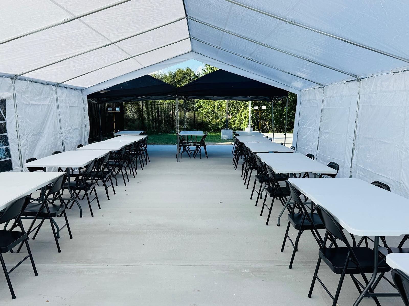 Outdoor event tent with rows of white tables and black folding chairs on a concrete surface.